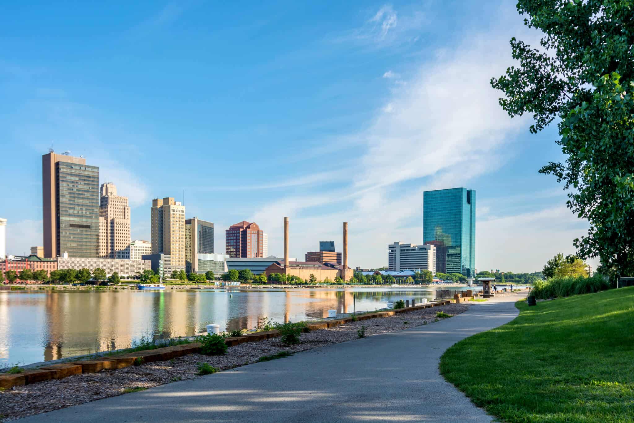 A panoramic view of downtown Toledo Ohio's skyline from across the Maumee river at a popular local park. A beautiful blue sky with white clouds for a backdrop.